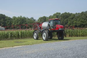 large red spraying tractor with booms and corn field
